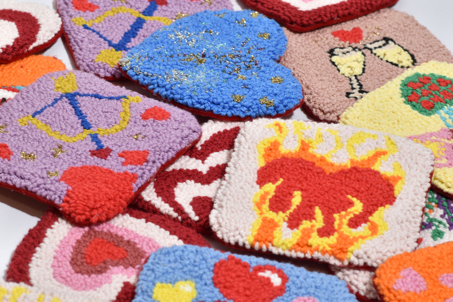 A collection of colorful handmade punch needle coasters with various embroidered designs including hearts, stars, and floral patterns.