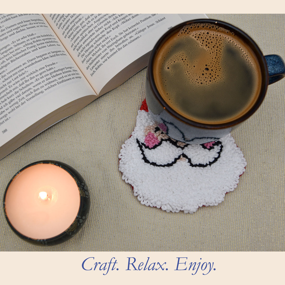 A cozy flat-lay scene featuring a white Punch needle Santa coaster , holding a dark coffee mug. An open book and a lit candle are placed nearby on a beige fabric surface, with the text 'Craft.