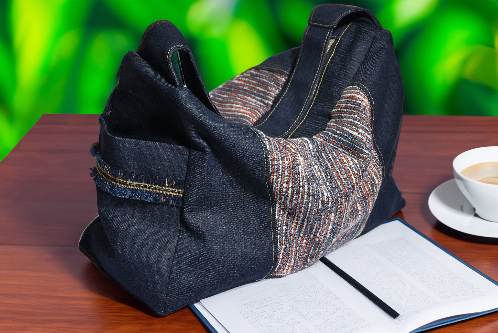 Navy blue jeans and patterned knitted fabric bag on a wooden surface with a blurred green background