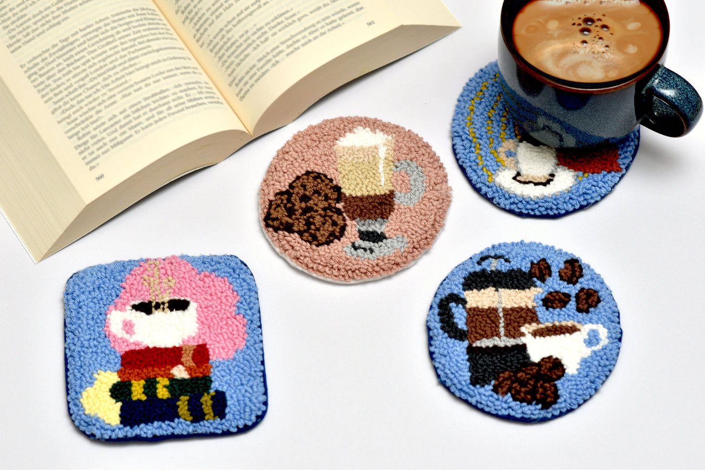 Set of four coasters with coffee-themed designs on a white surface with a book and mug.