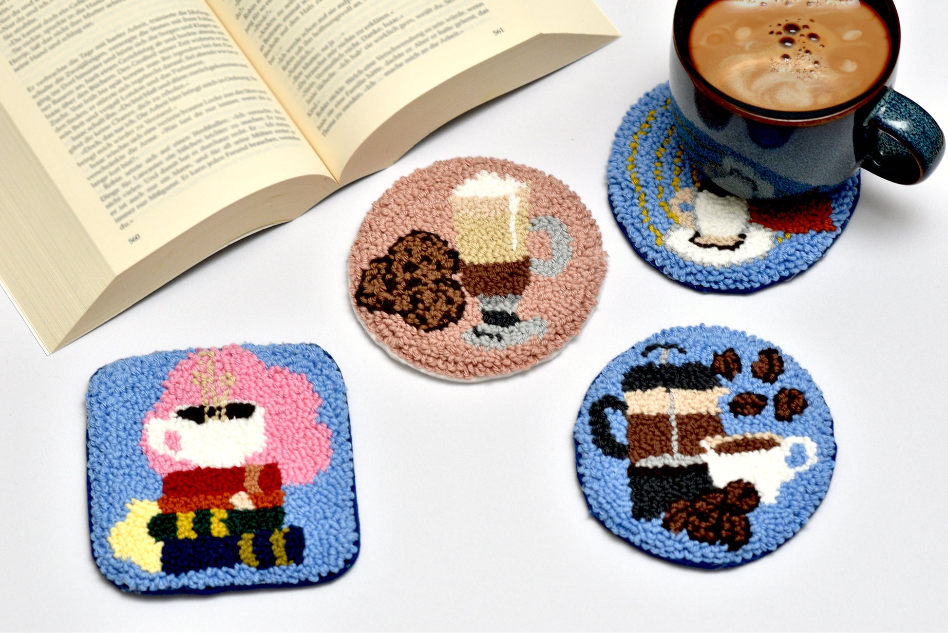 Set of four coasters with coffee-themed designs on a white surface with a book and mug.