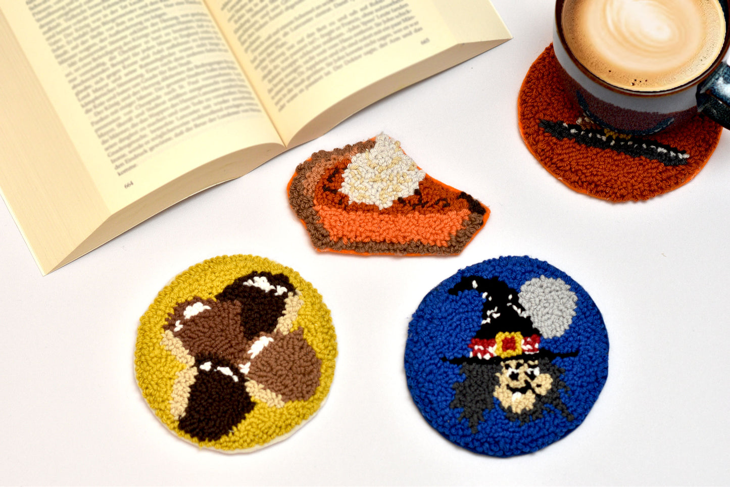 Three colorful coasters with autumn-themed designs on a white surface with a book and coffee cup.
