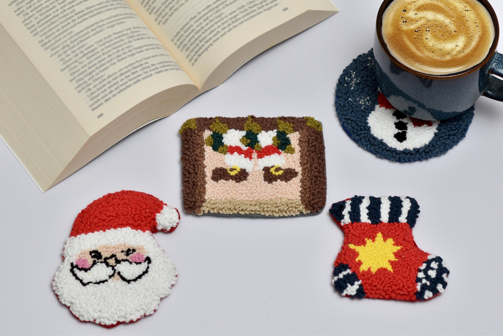 Three colorful punch needle coasters shaped like a santa face, a santa stuck in chimney design, and a christmas stocking with a book and coffee cup.