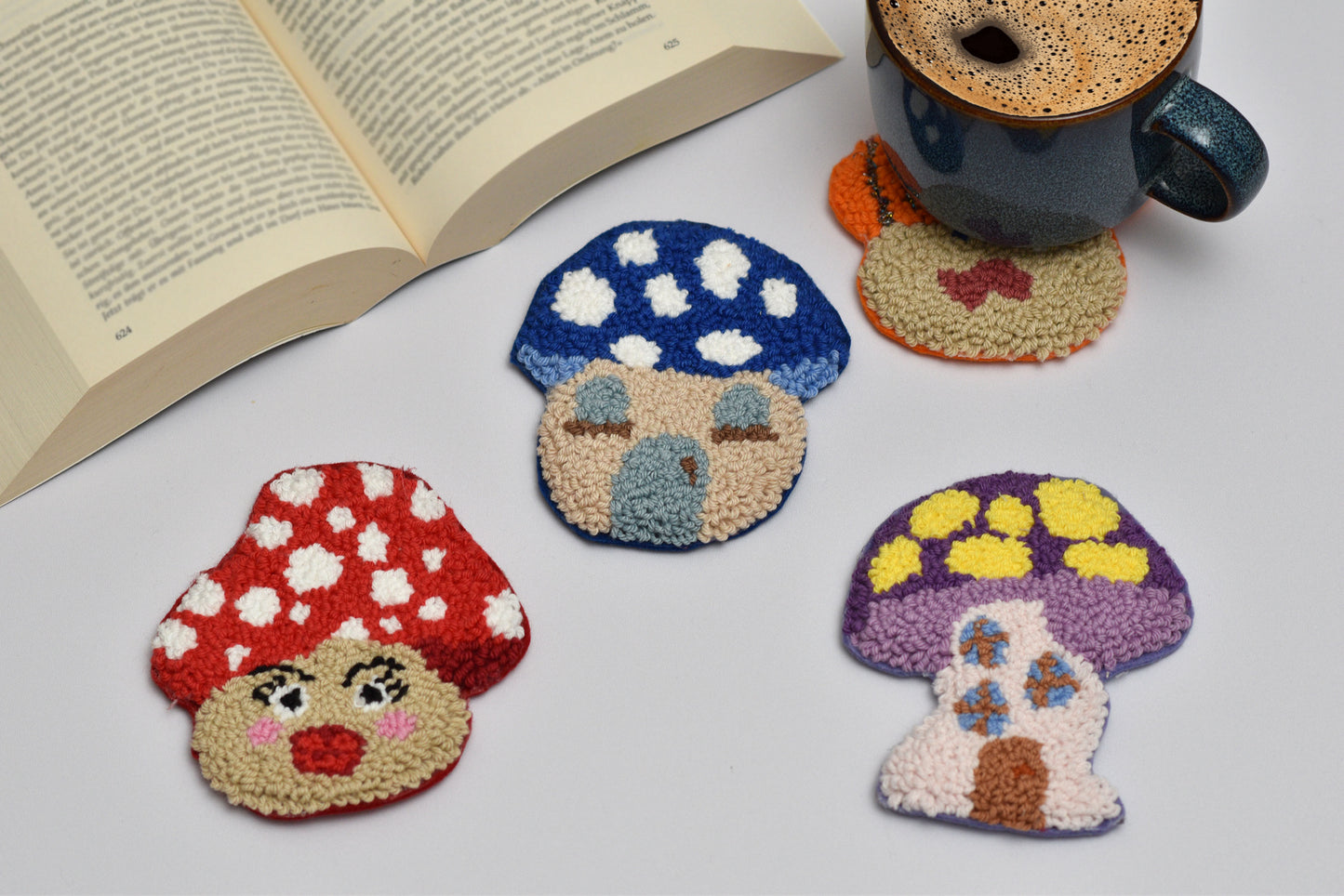 Colorful mushroom-shaped punch needle coasters on a white surface with a book and mug.