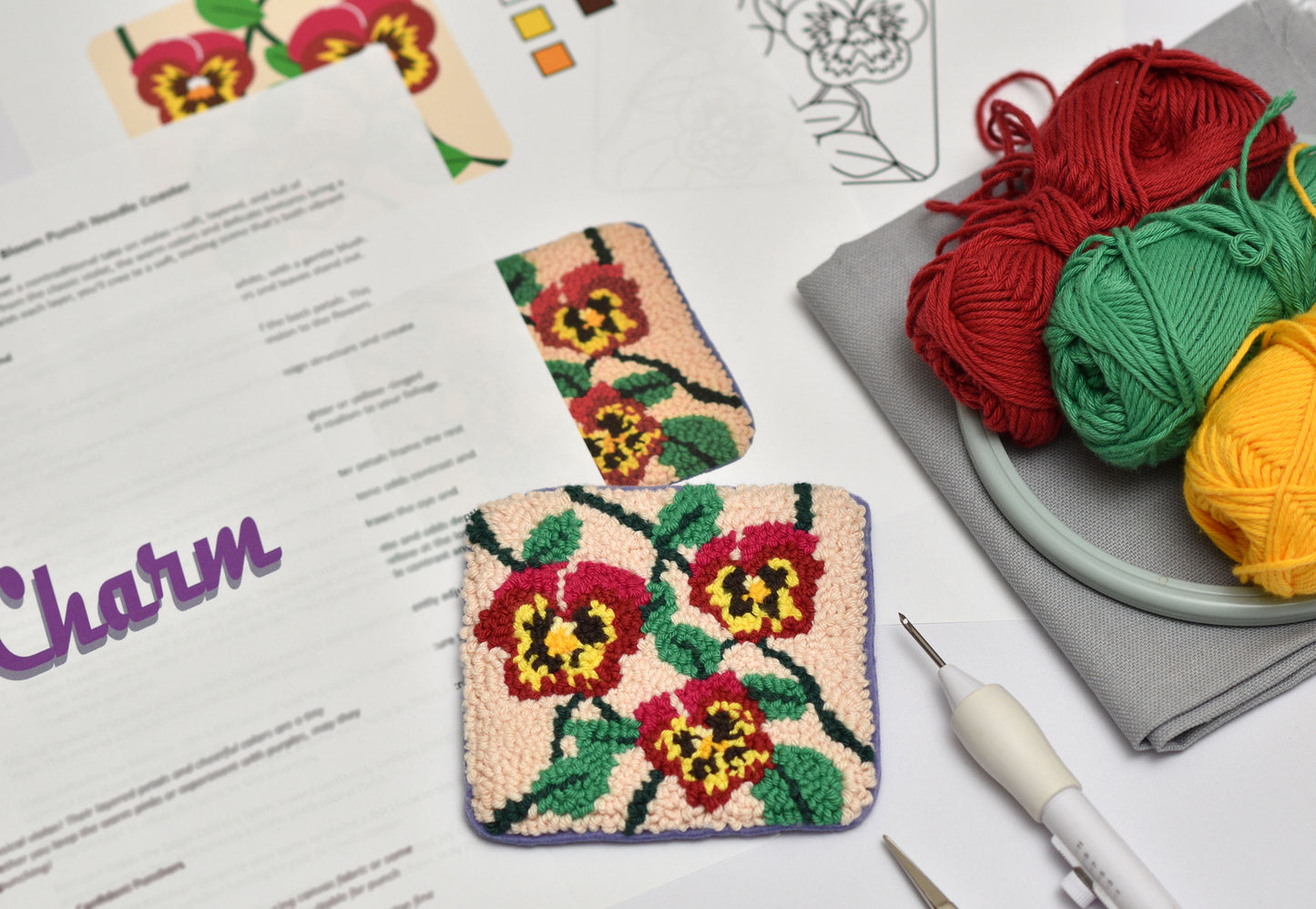 Two floral-patterned embroidered coasters on a surface with yarn and a pattern sheet.