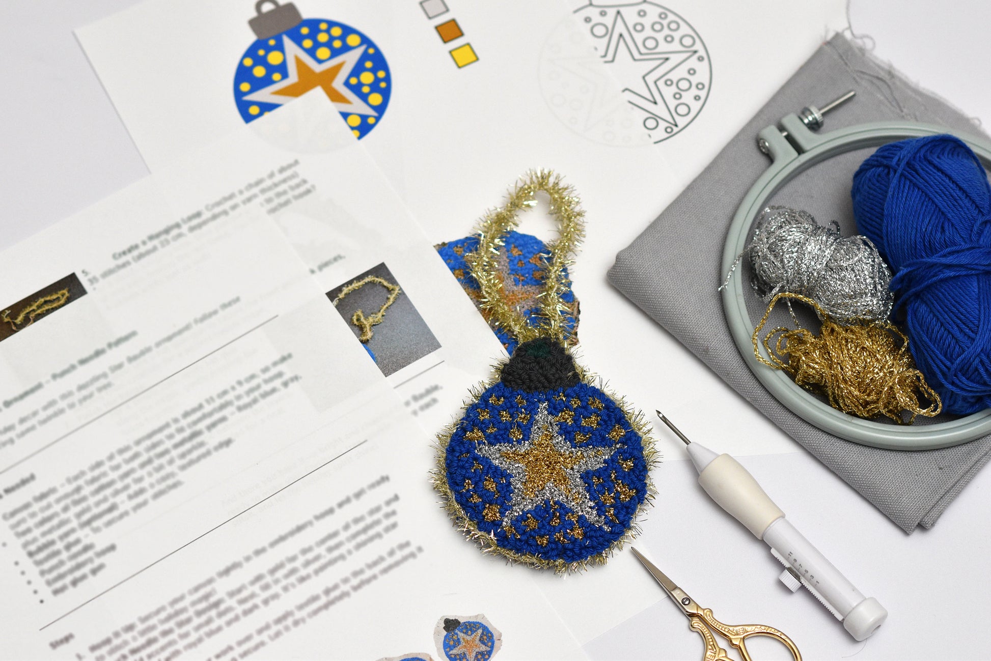 Punch needled ornament with Embroidery hoop with blue and gold thread, scissors, and a letter on a white surface
