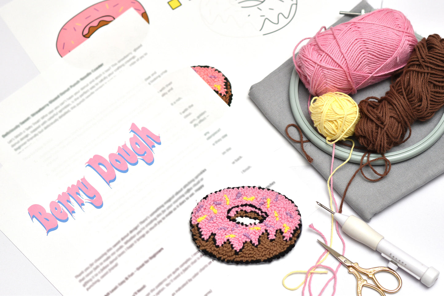 Punch needle donut  coaster with yarn, scissors, and a pattern sheet on a white background