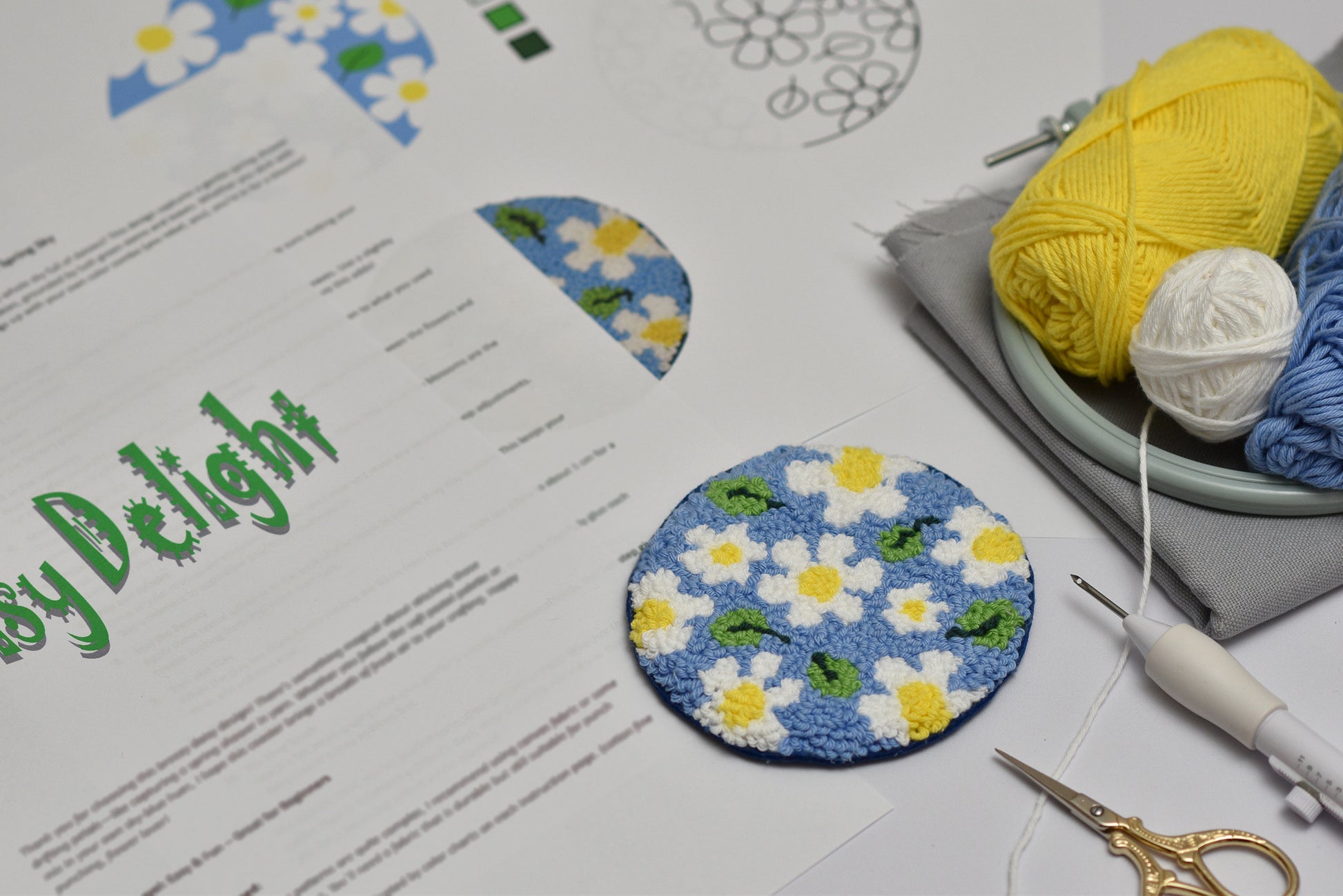 Embroidery hoop with floral design, yarn, scissors, and pattern sheet on a table.