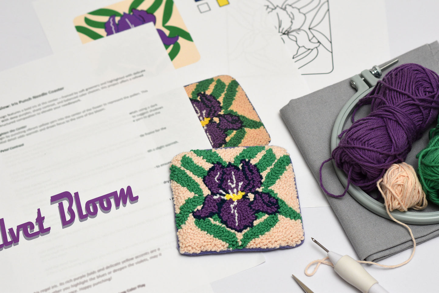 Two embroidered coasters with floral iris designs on a table with yarn and tools.