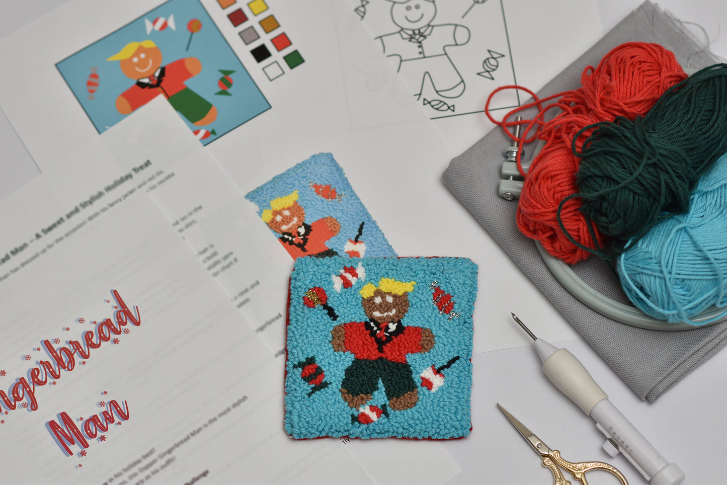 Punch needled gingerbread man design coaster on fabric with yarn and tools on a table.