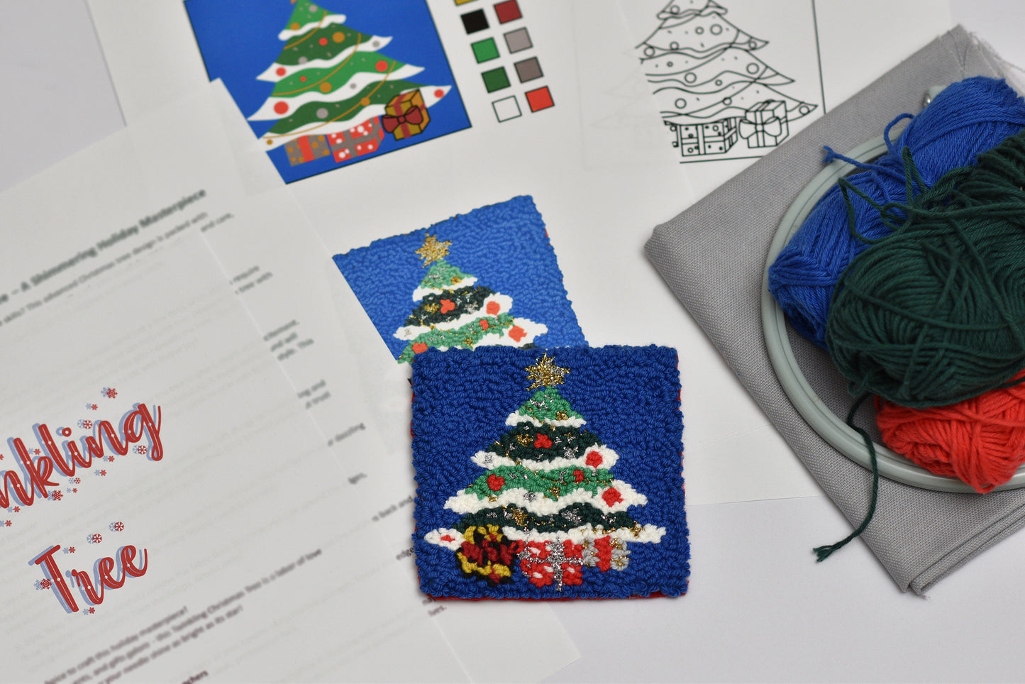 Punch needled coaster with Christmas tree design on blue fabric with yarn and pattern sheet in the background