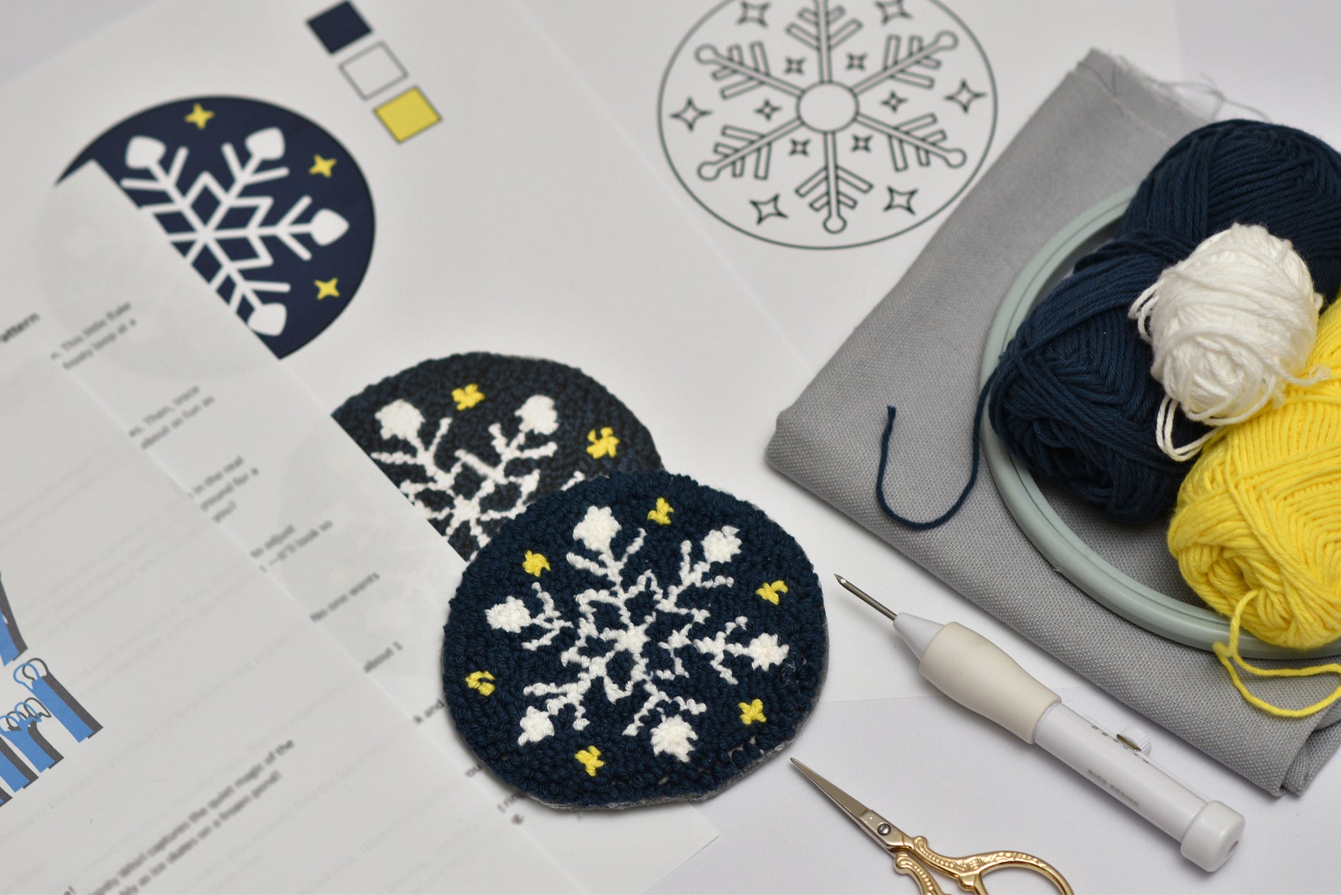 Embroidery coaster project with snowflake designs on fabric, yarn, and sewing tools.