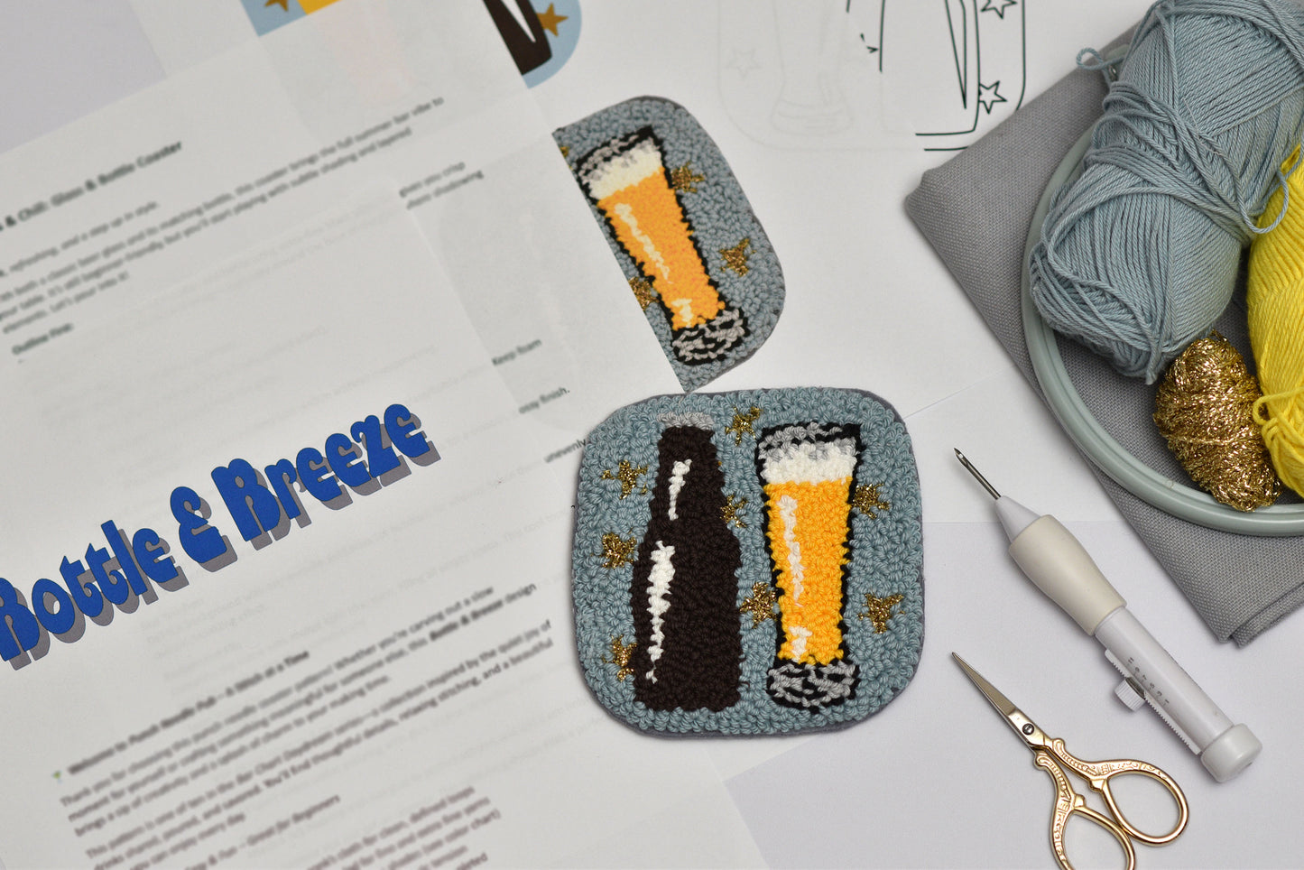 Two embroidered coasters with beer and bottle designs on a table with crafting supplies.