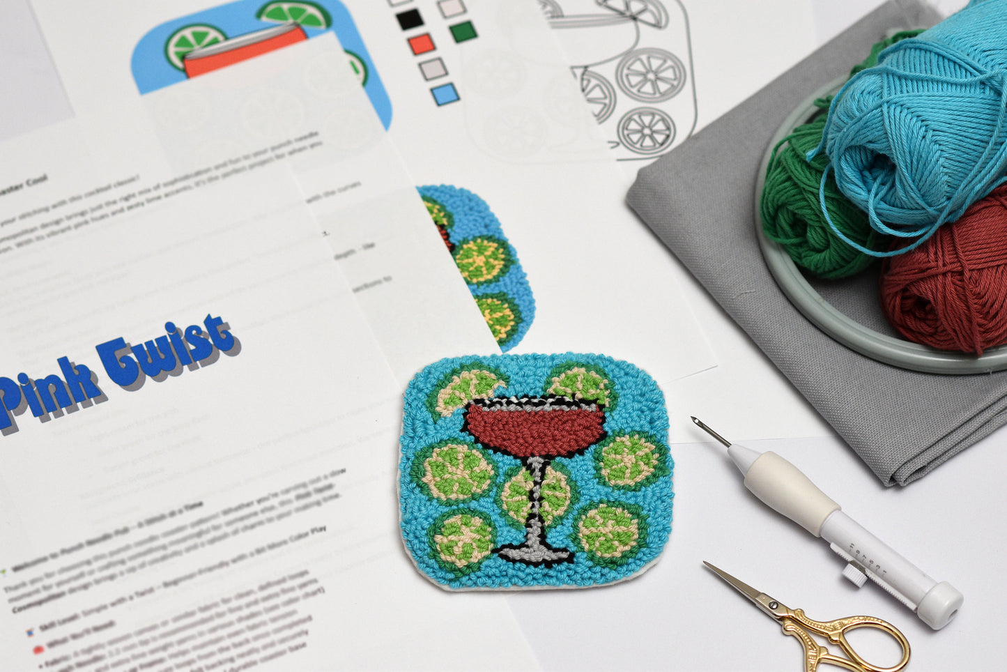 Embroidery hoop, a punch needle coaster  with a cocktail design, yarn, and sewing tools on a table.