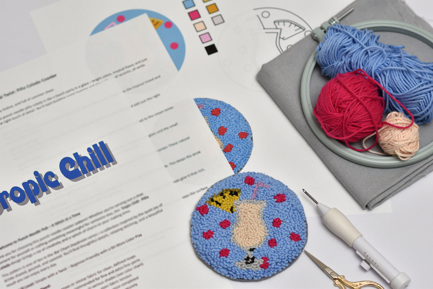 Embroidery hoop. embroidered coaster with cocktail design, yarn, scissors, and printed pattern on a table