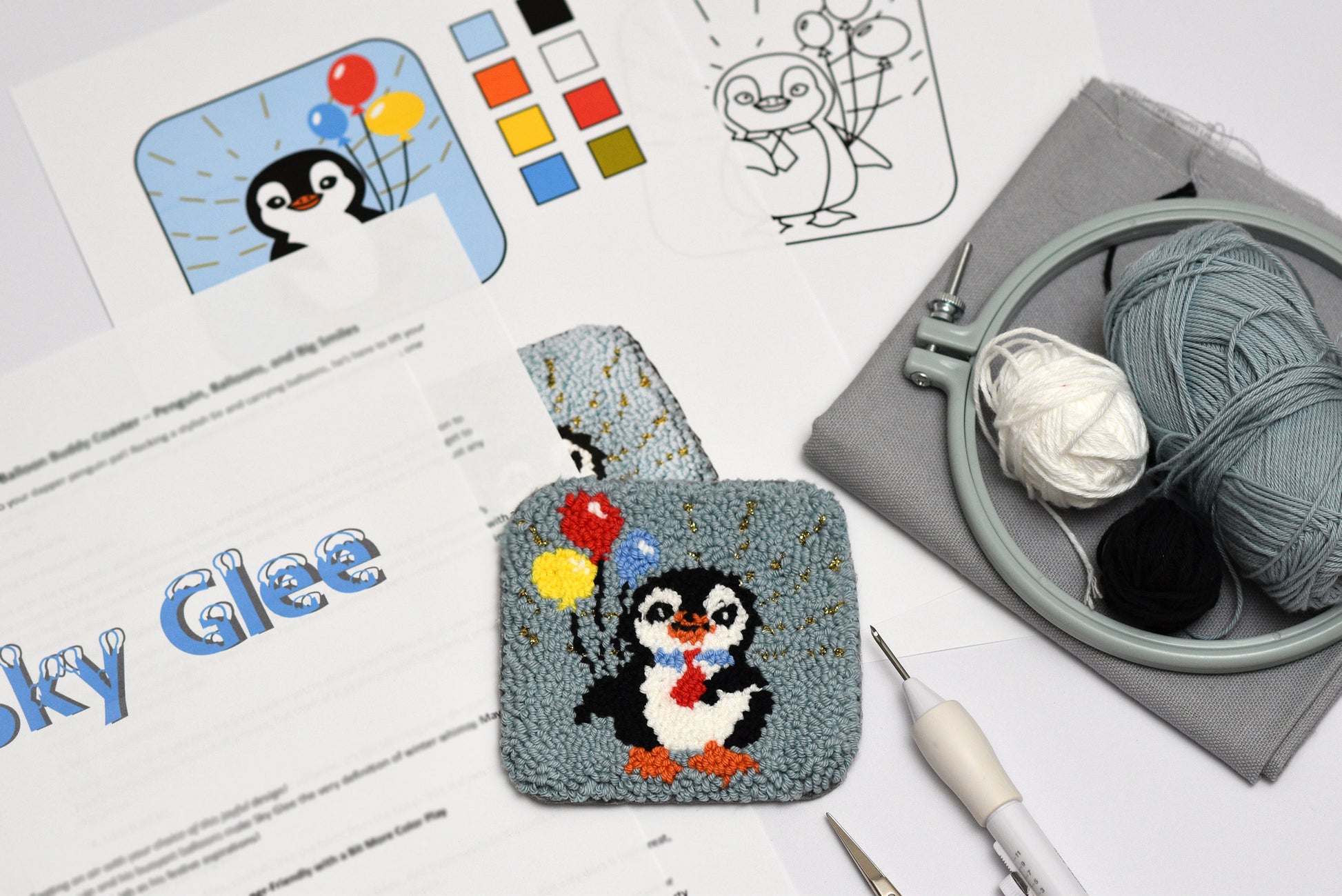 Punch needled penguin coaster design on a case with yarn and tools on a table