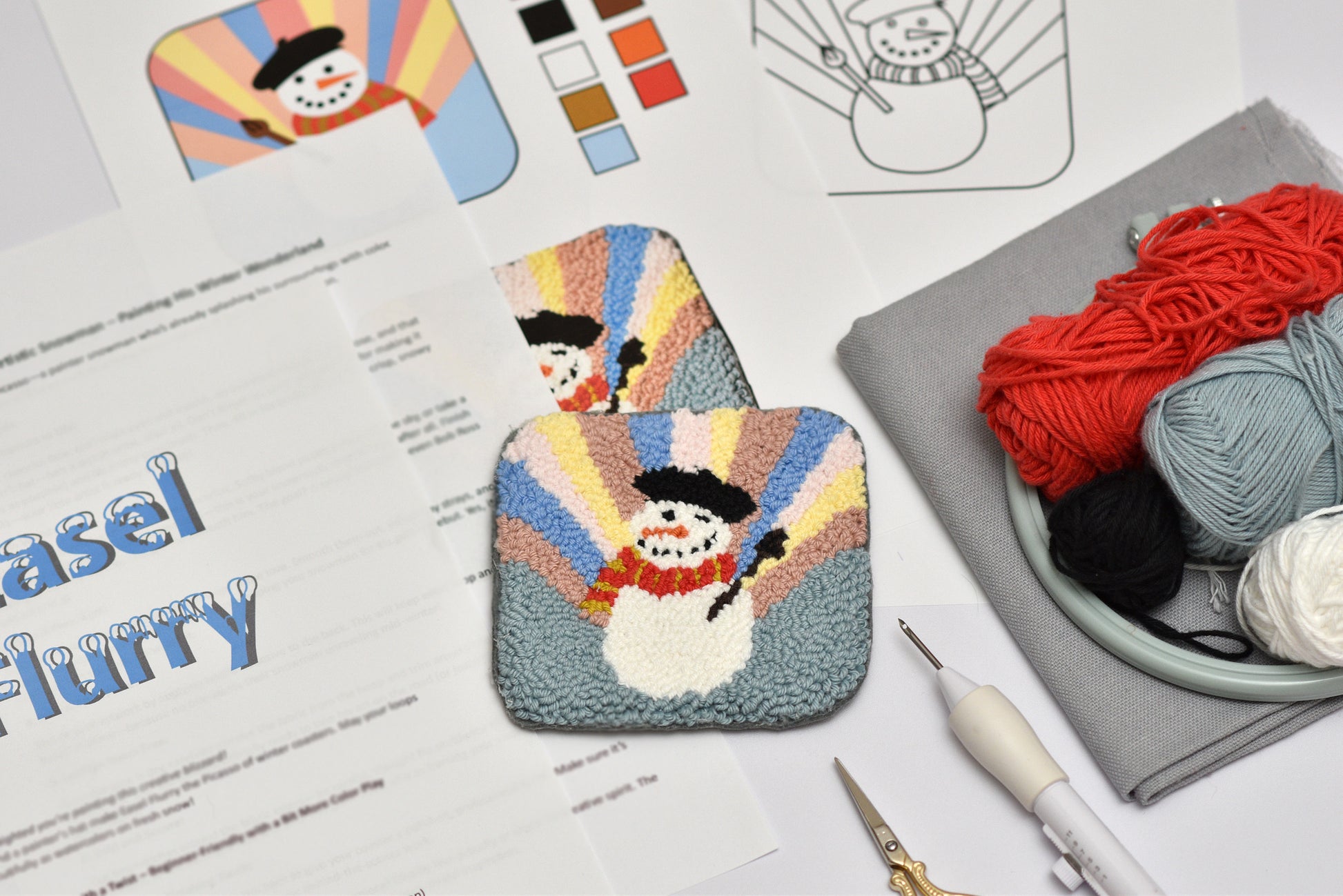 Embroidered snowman coaster with yarn and tools on a table