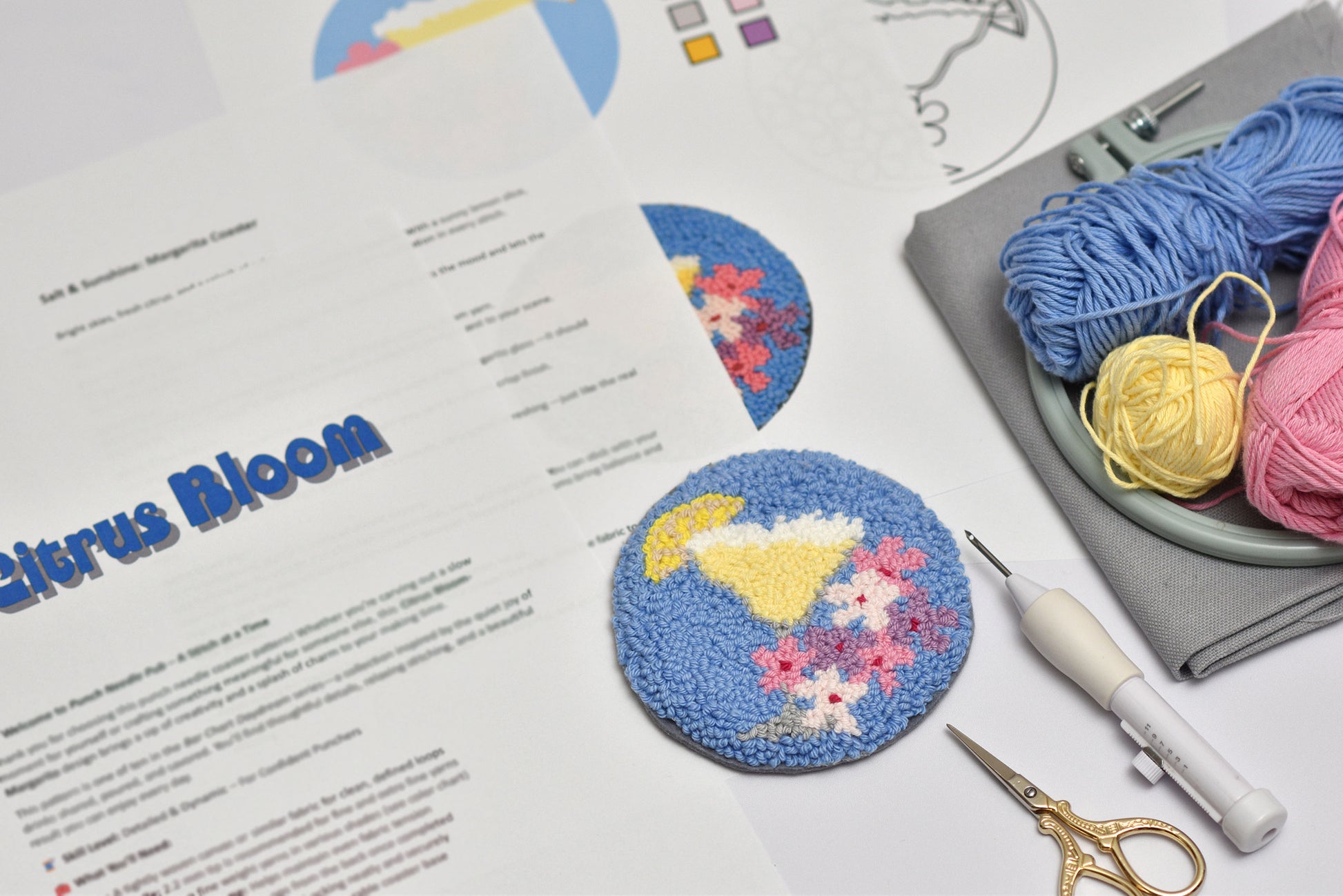 Embroidery hoop with Margarita cocktail design, yarn balls, and sewing tools on a table with printed instructions.