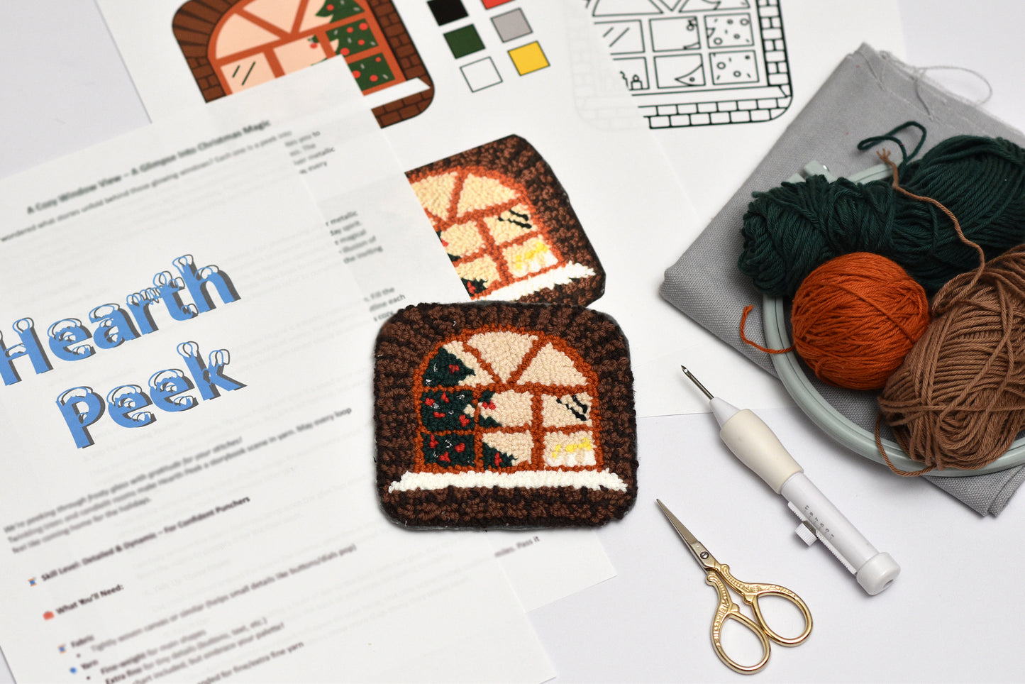 Punch needled house-shaped coaster with yarn and tools on a table