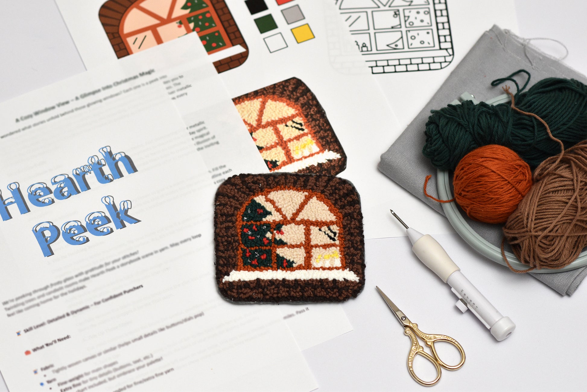 Punch needled house-shaped coaster with yarn and tools on a table