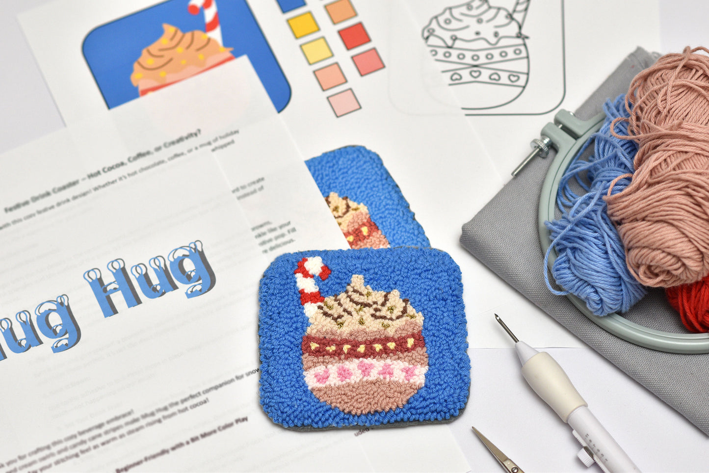 Embroidery hoop with yarn, completed embroidered coaster, and design sheet on a table.