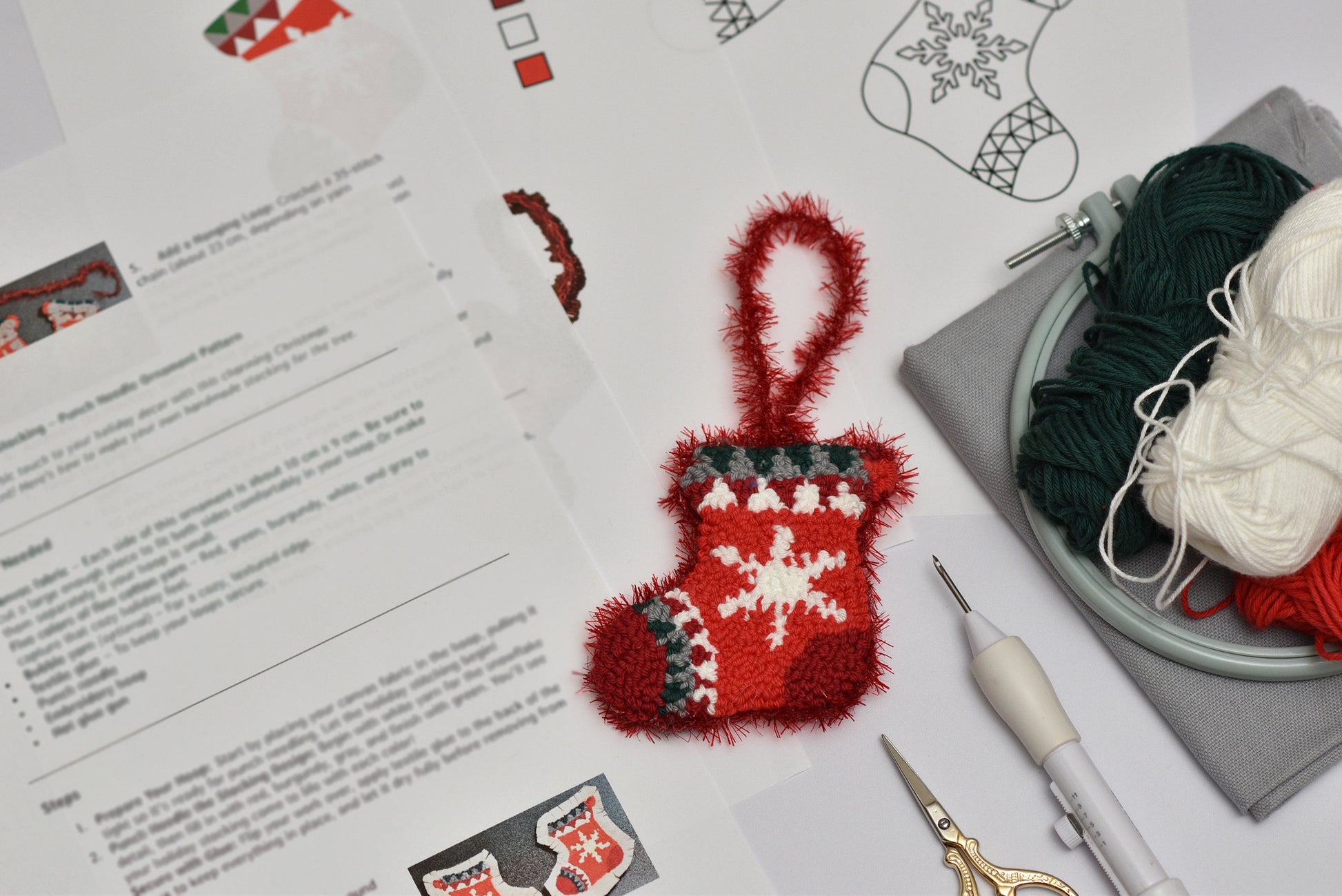 Small red punch needled stocking with a snowflake design on a table with yarn and knitting tools.