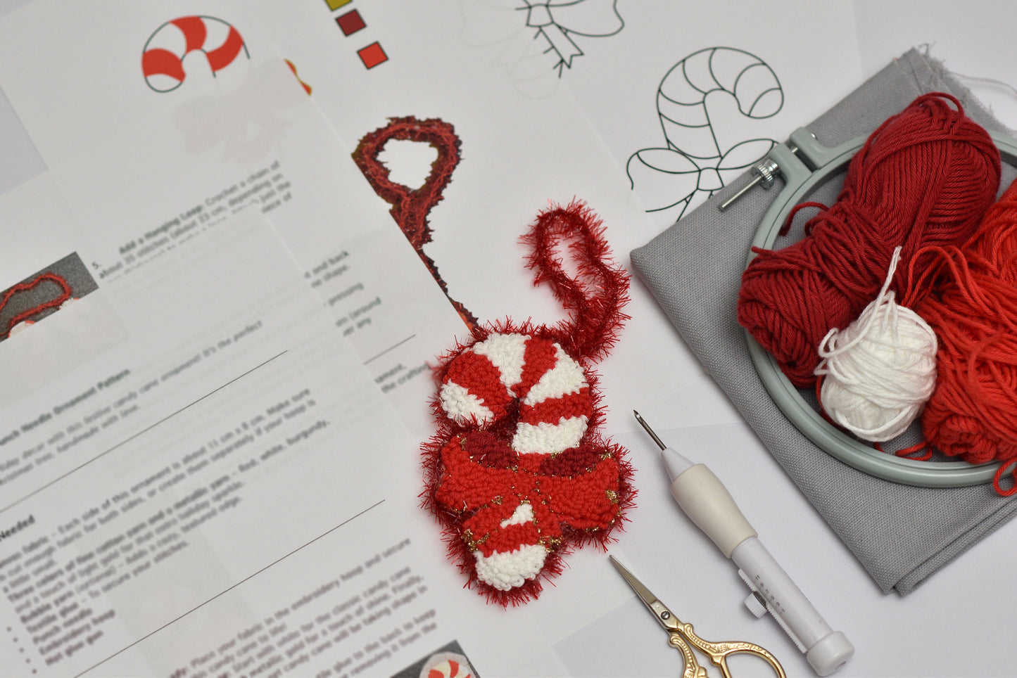 Embroidery hoop with red and white yarn, scissors, and a completed red and white embroidered candy cane design on a paper with text.