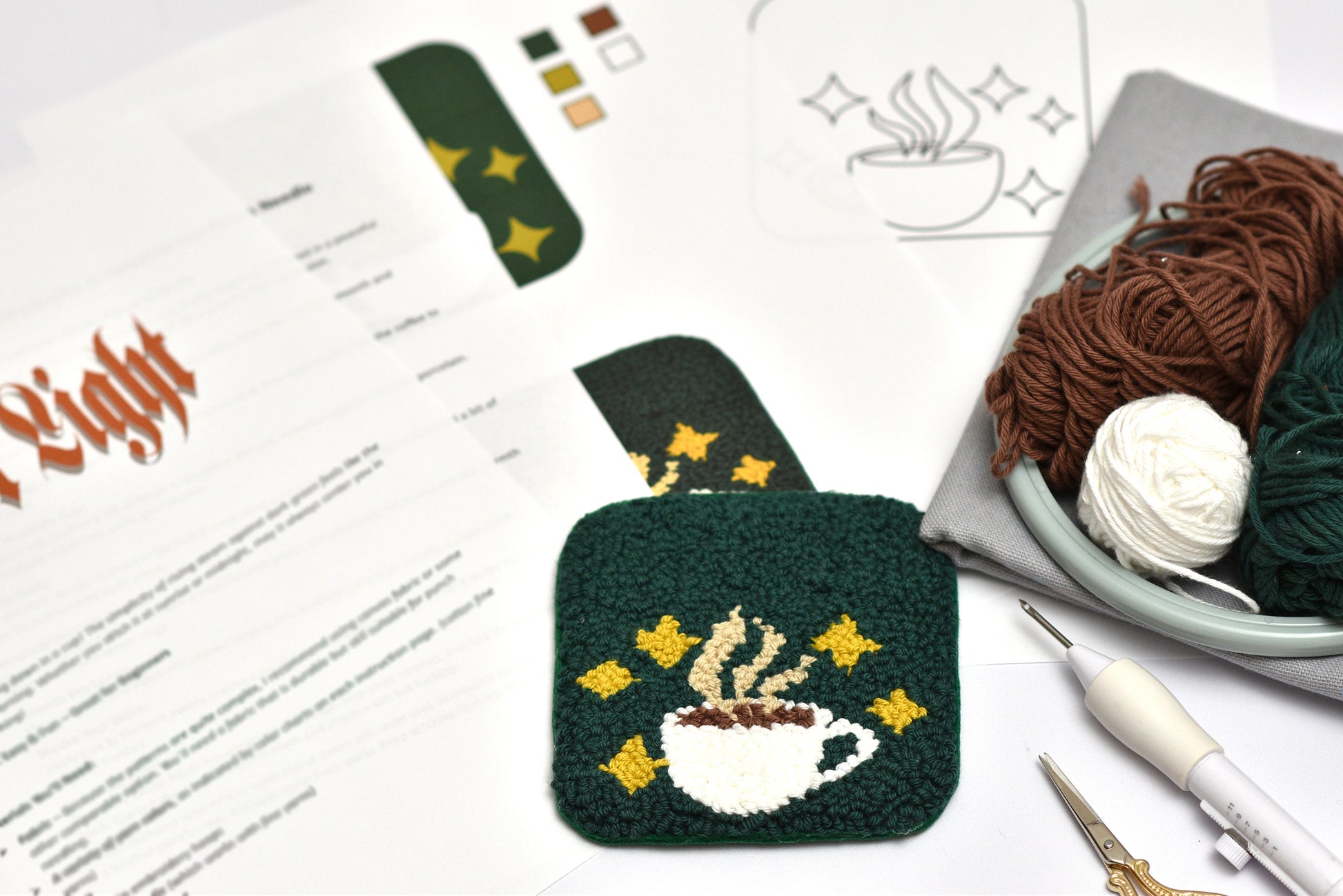 Punch needled coaster with coffee design on a table with yarn and tools