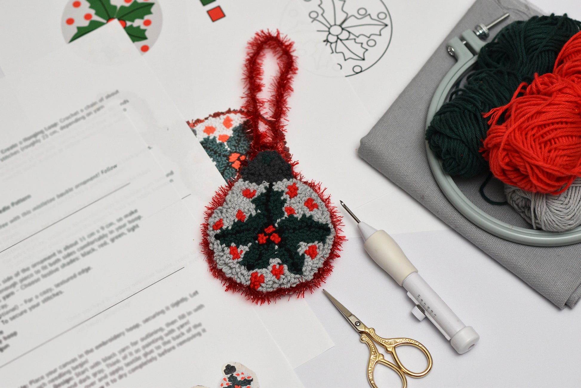 Embroidery hoop with red yarn, scissors, and a completed embroidered mistletoe design on a white surface.