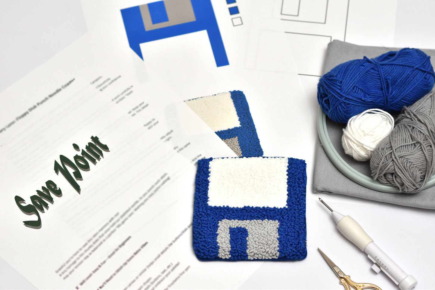 Punch needled floppy disc designed coaster with yarn and tools on a table