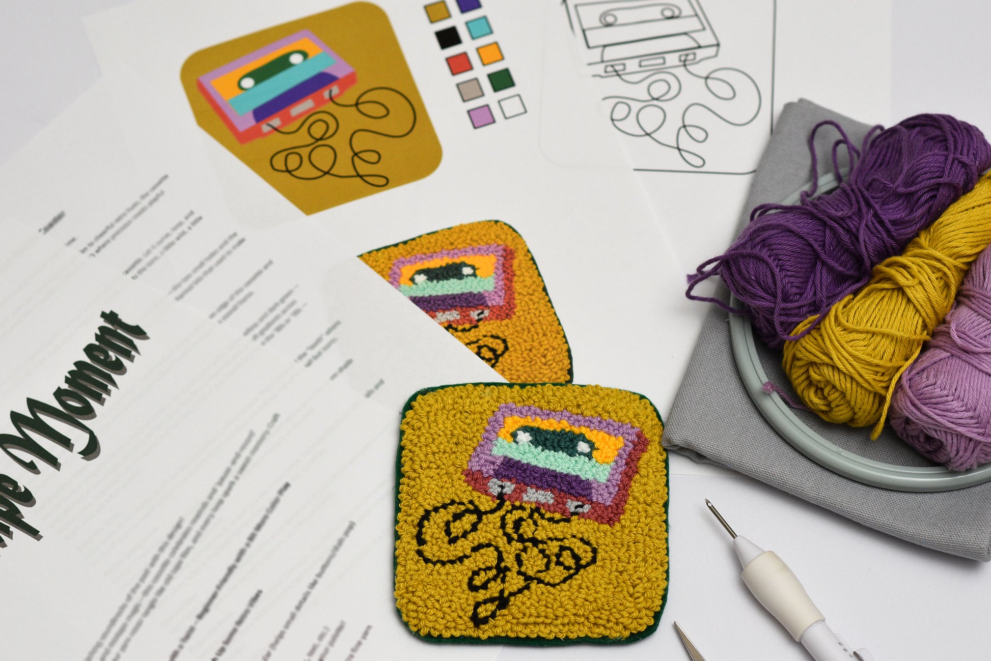 Punch needle coaster with colorful retro cassette design on a table with yarn and patterns.
