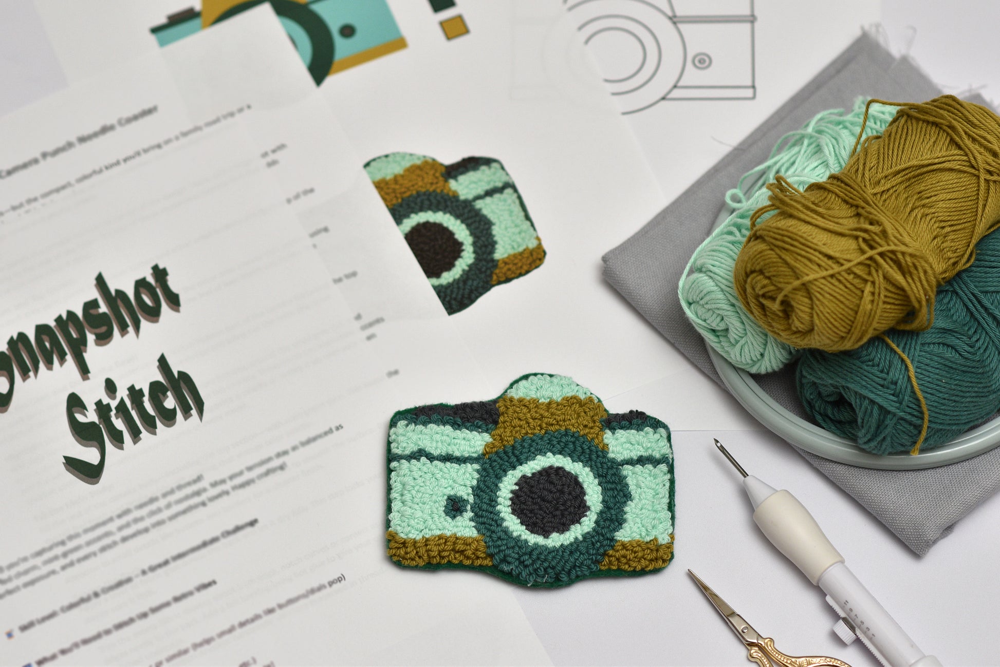 Punch needle camera coaster pattern on a table with yarn and tools