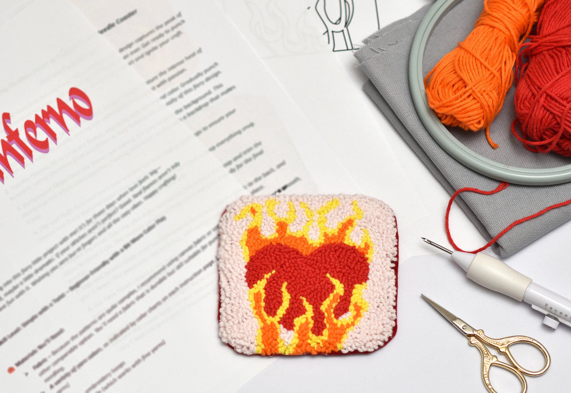 Embroidery project with heart design, yarn, scissors, and pattern sheet on a white surface