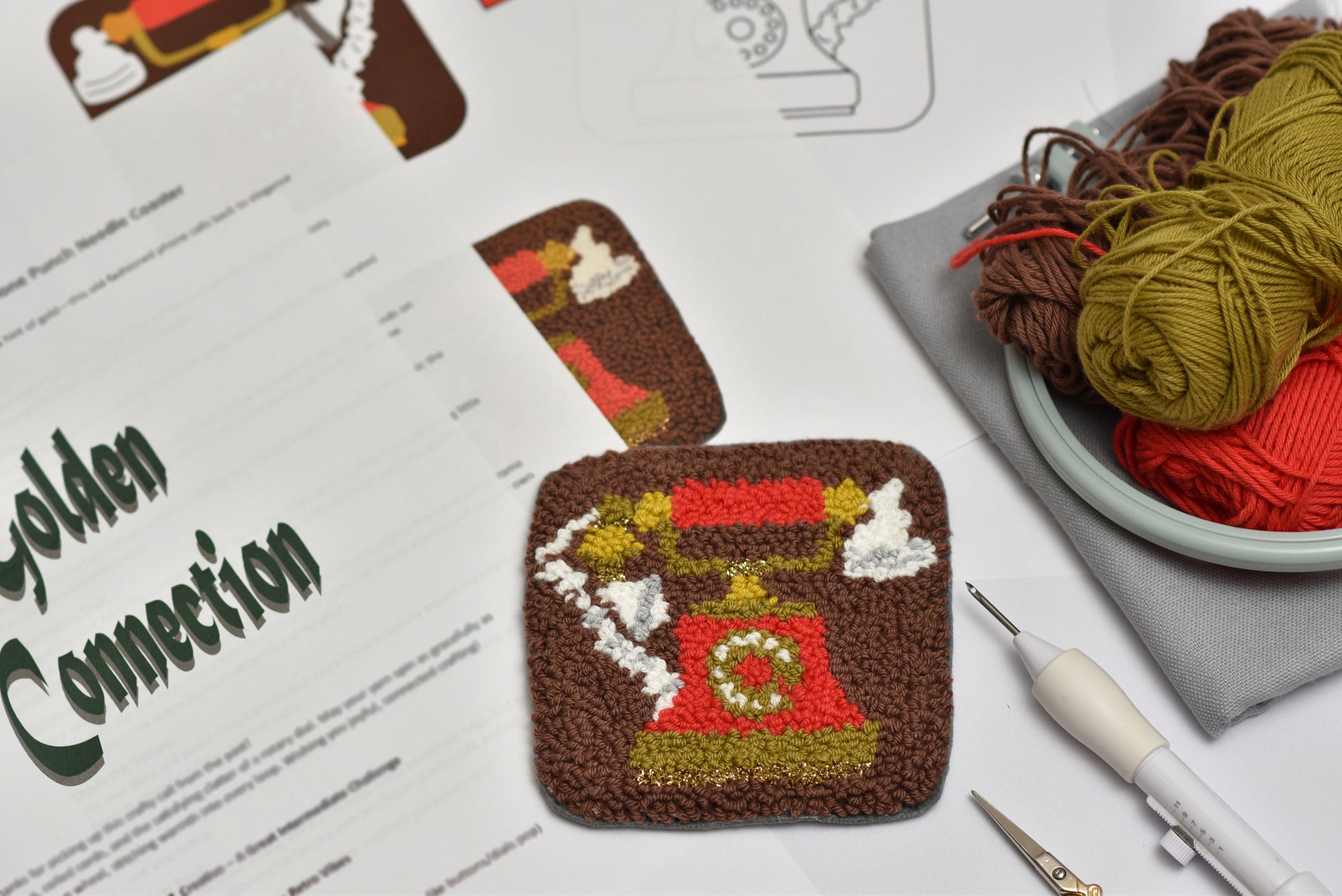 Punch needle phone shaped coaster on a table with yarn and tools