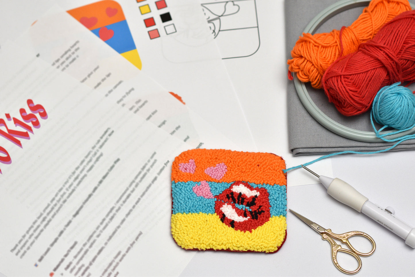 Colorfulpunch needled coaster with mouth design on a table with yarn and knitting tools.