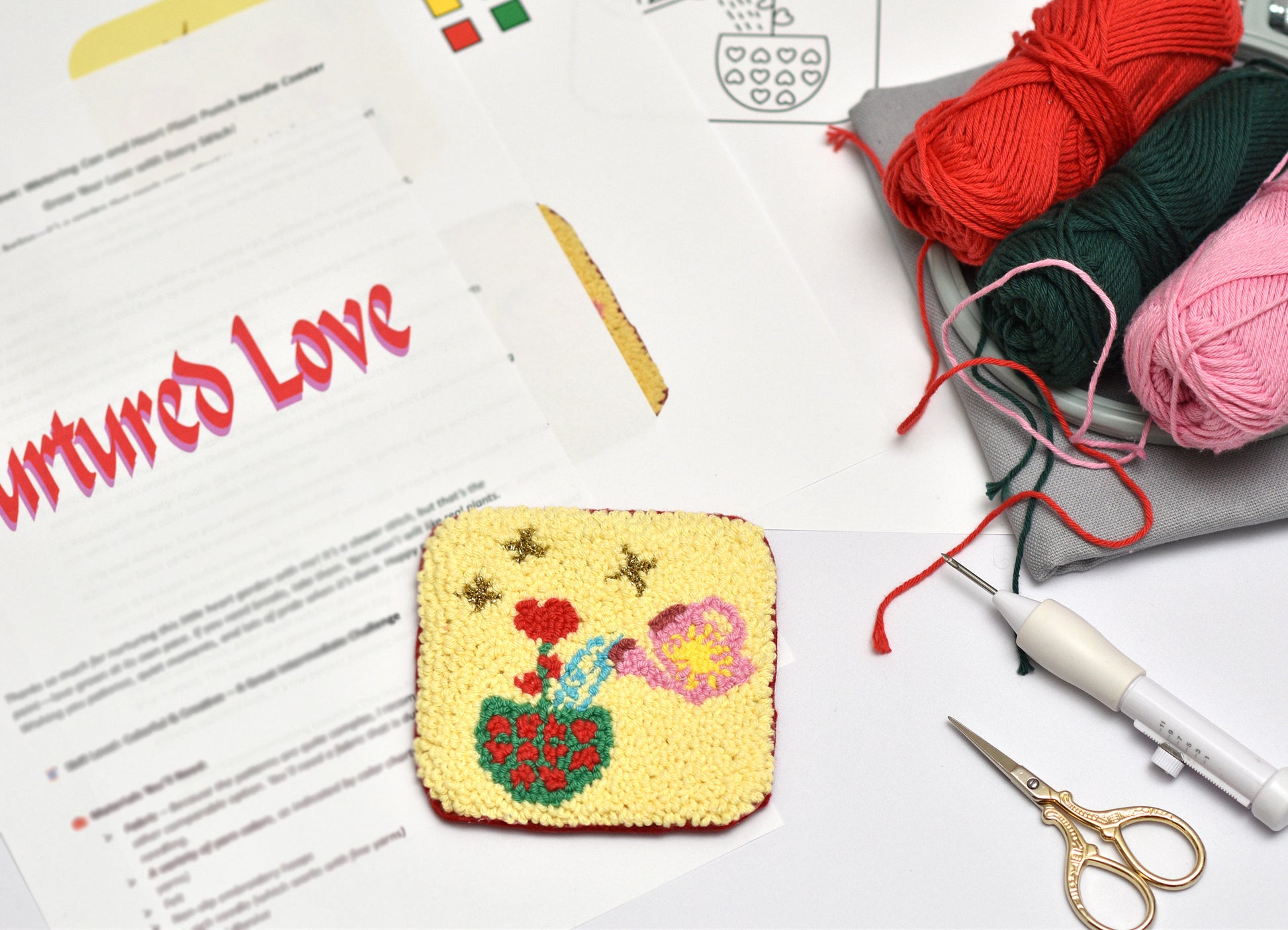 Embroidered coaster with flowers on a table with yarn, scissors, and a needlework pattern sheet.