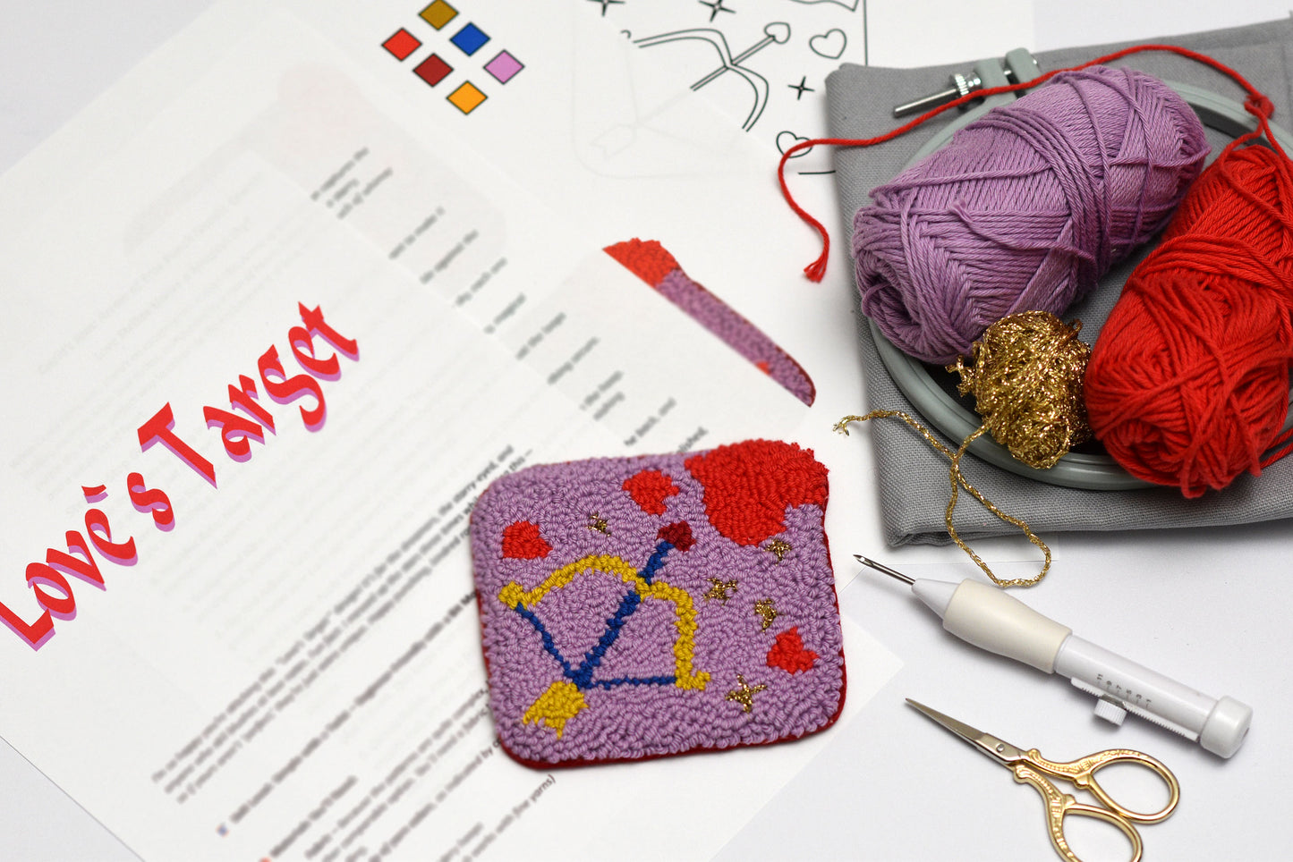 Punch needle swatch with colorful patterns on a table with yarn and tools.