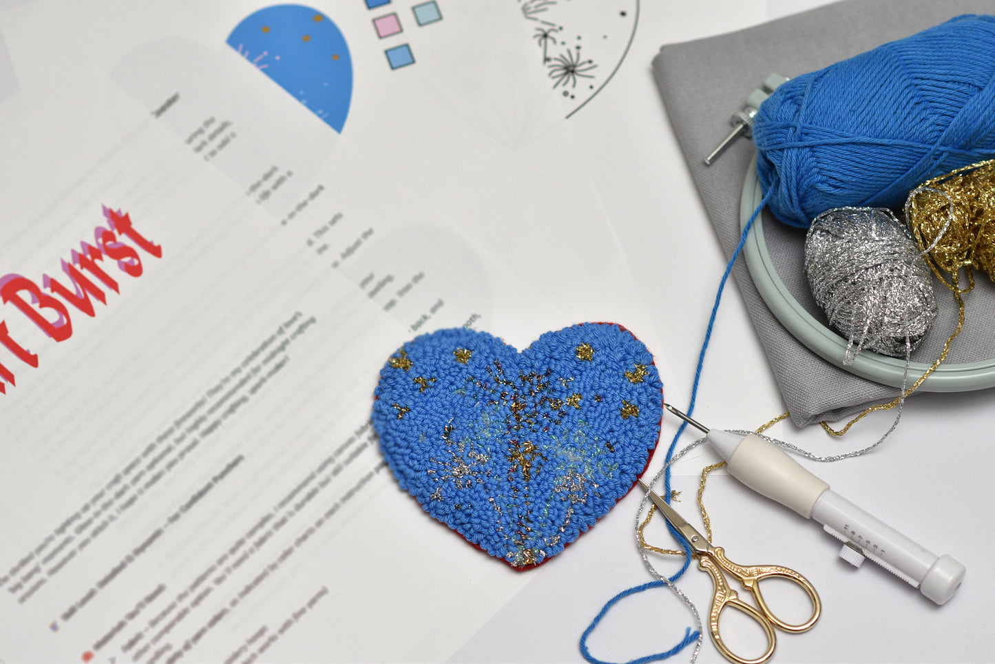 Blue embroidered heart with cross-stitching tools and yarn on a table