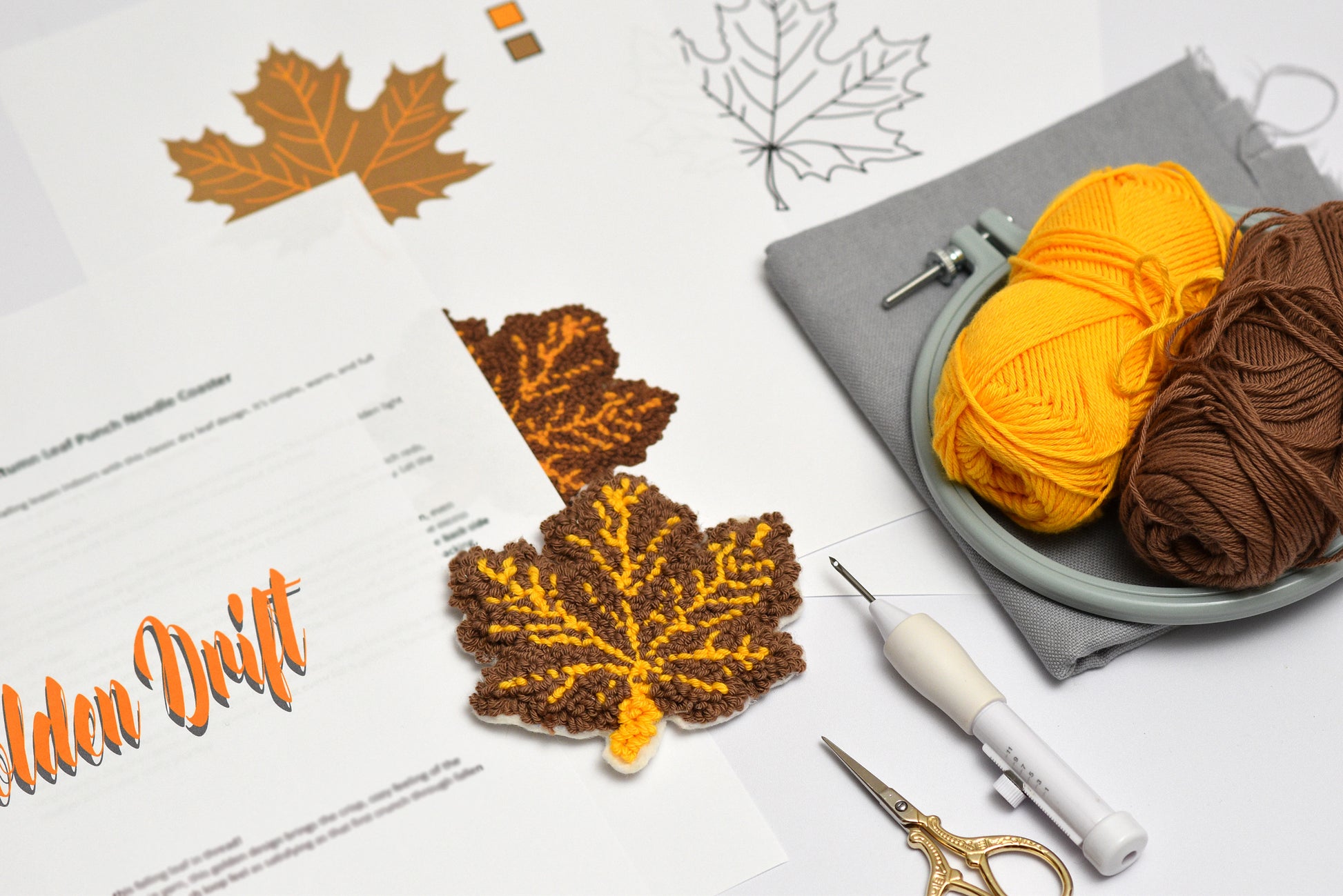 Punch needled leaves, yarn, knitting needles, and scissors on a table with 'Autumn Drift' text.