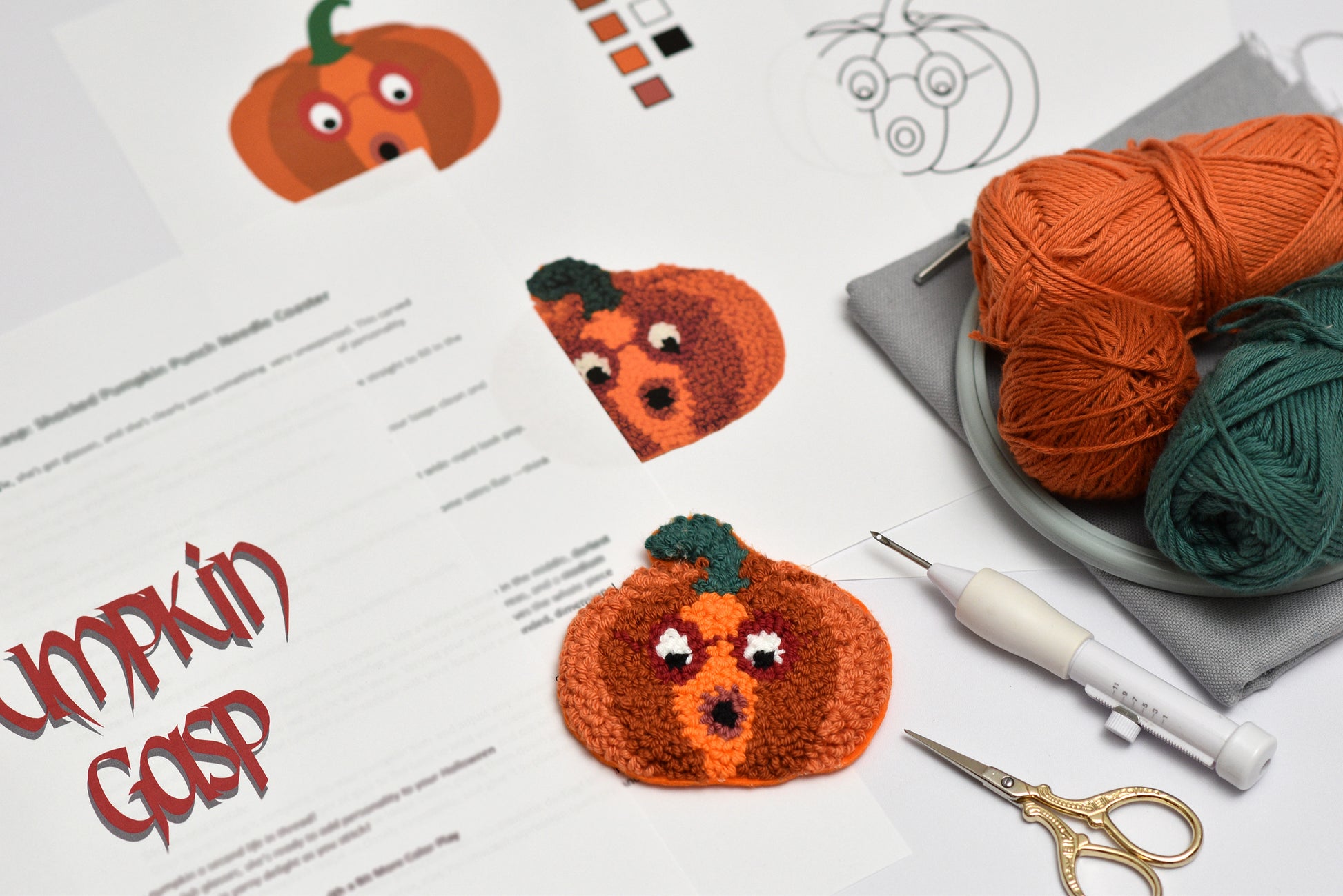 Punch needled pumpkin coaster with yarn, punch needle hook, and scissors on a table.