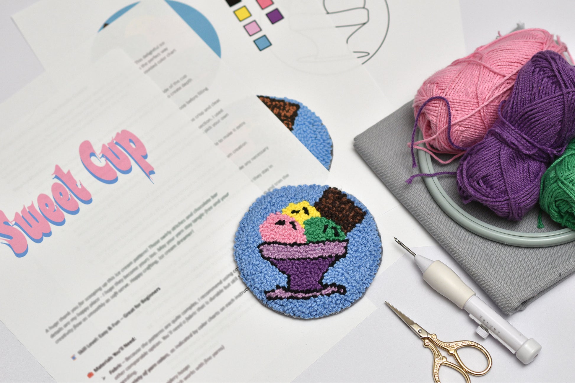 Punch needle ice cream cone on a white surface with yarn and tools.