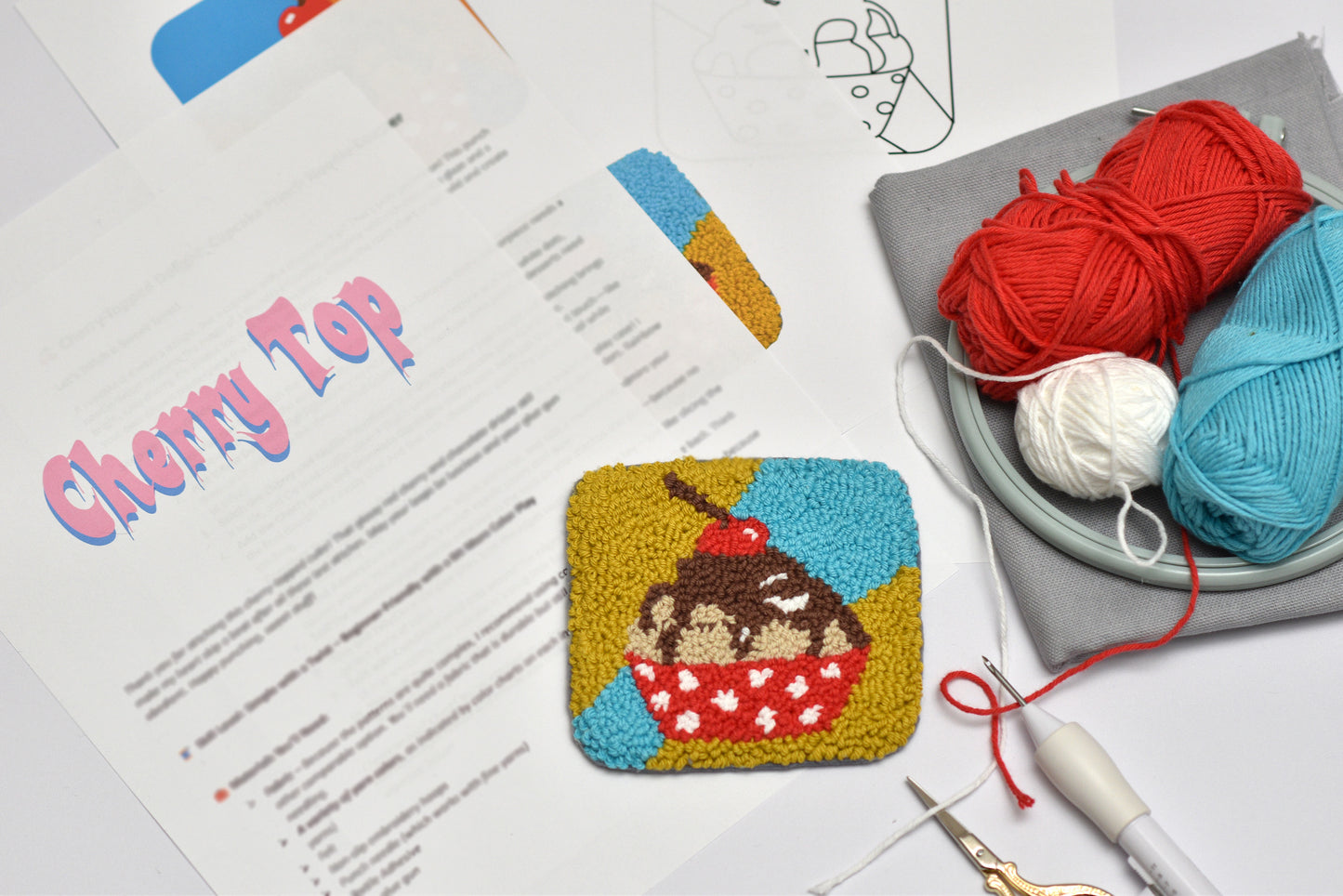 Punch needle coaster cup cake design  with yarn and tools on a table
