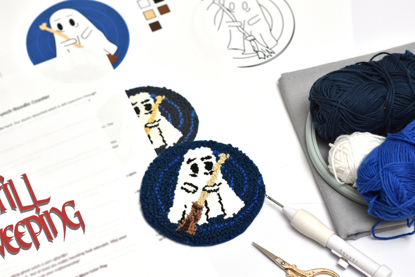 Embroidery coaster project with ghost design, yarn, and sewing tools on a white surface.