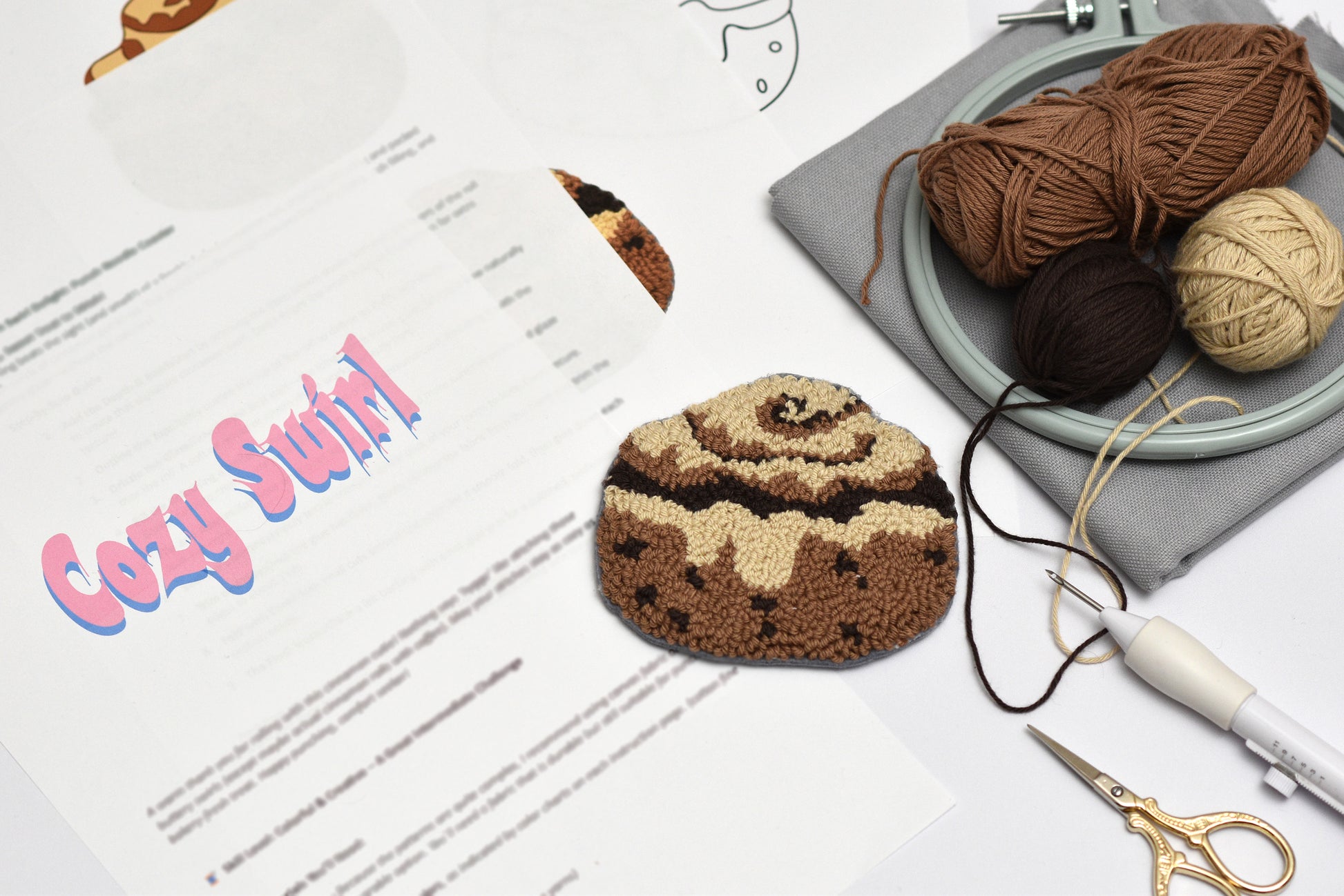 Embroidered coaster resembling a cinnamon roll on a table with yarn and knitting tools.