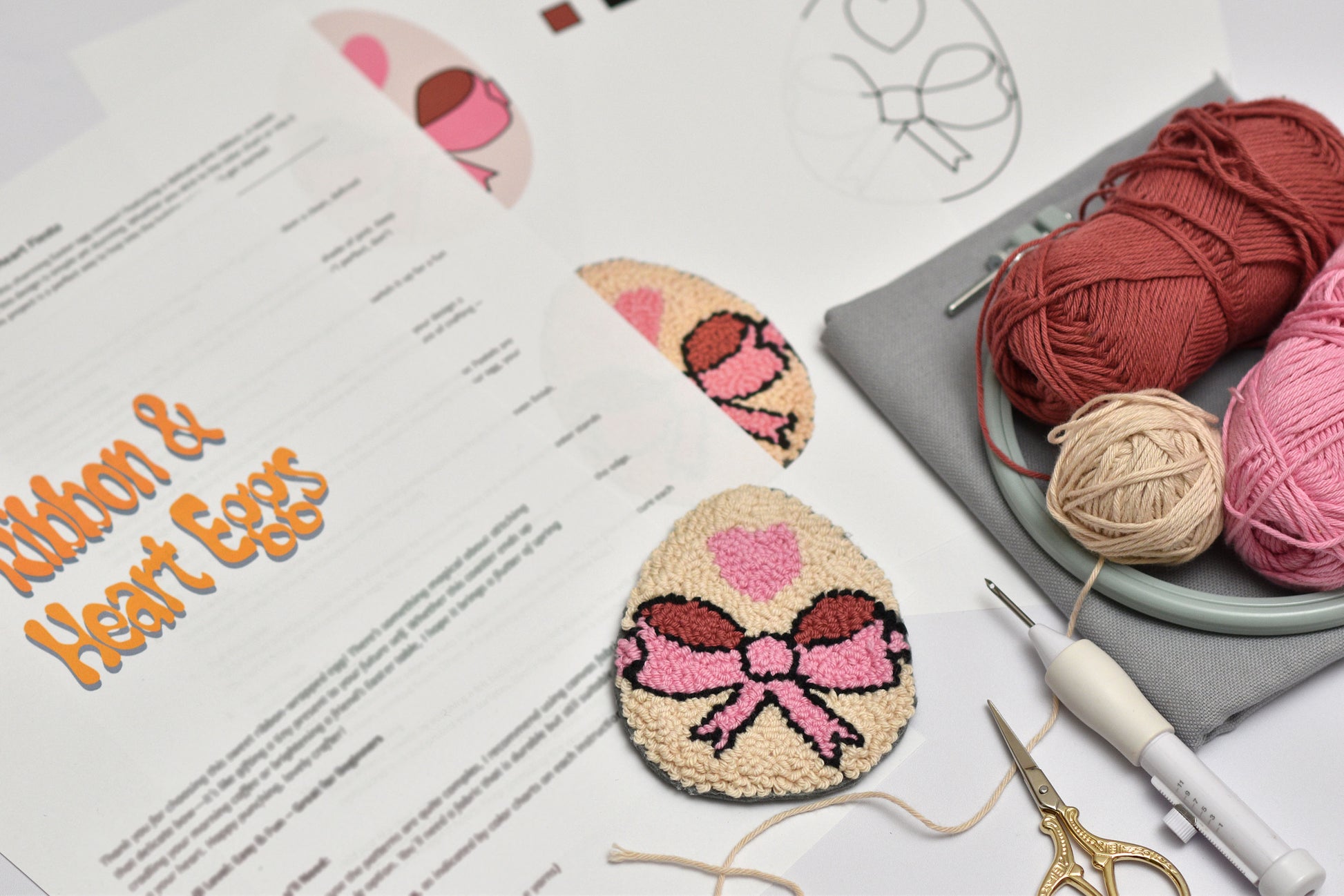 Embroidery hoop with yarn, embroidery tools, and embroidered egg coaster on a table with a pattern sheet.