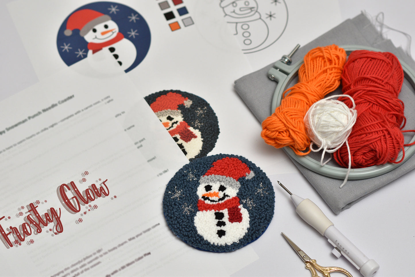 Snowman-themed punch needle project with yarn, scissors, and a punch needle hook a white surface.