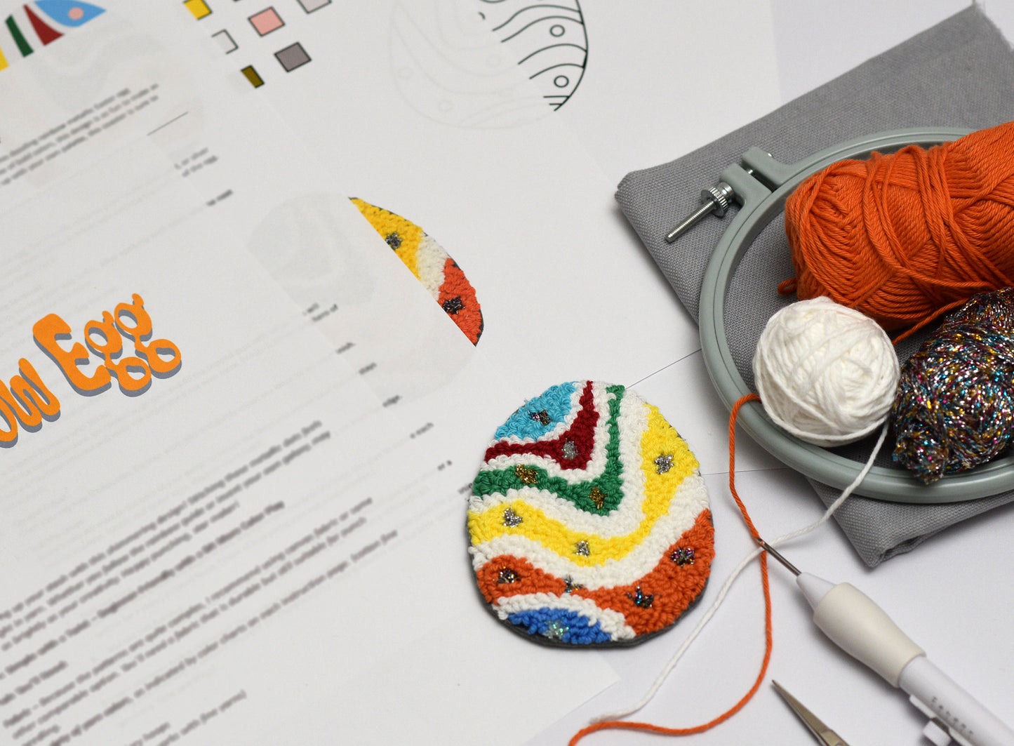 Colorful embroidered Easter egg on a table with embroidery hoop and yarn.