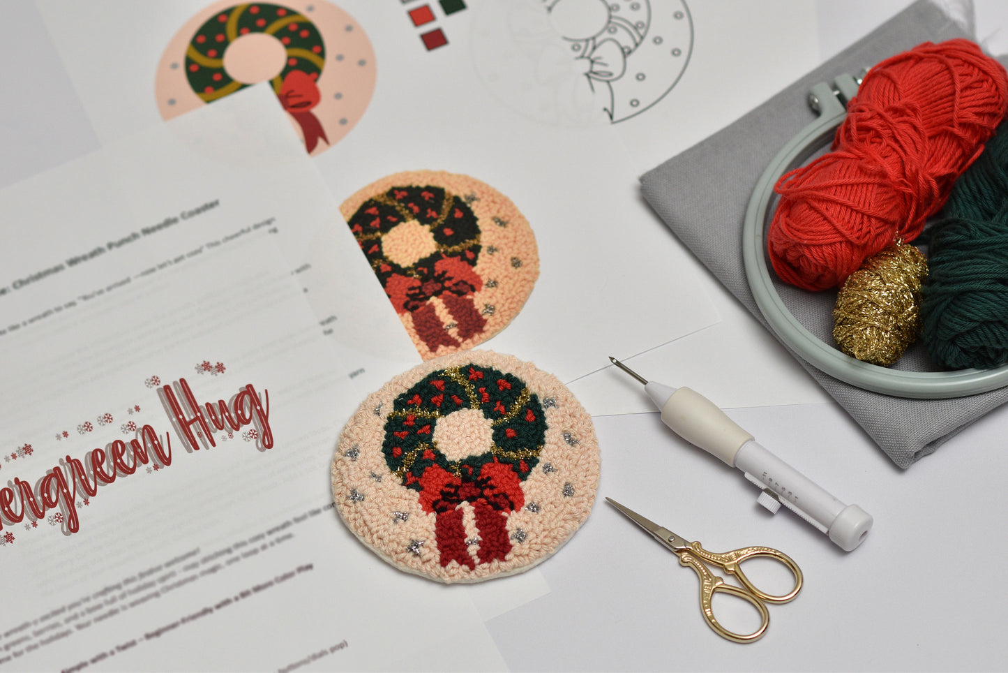 Embroidery hoop with red yarn, scissors, and embroidered coasters with wreath design on a white surface.