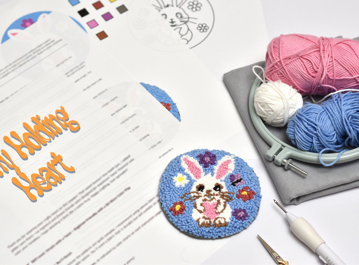 Embroidery hoop with yarn, completed embroidery coaster with Easter Bunny design, and design sheet on a white surface.