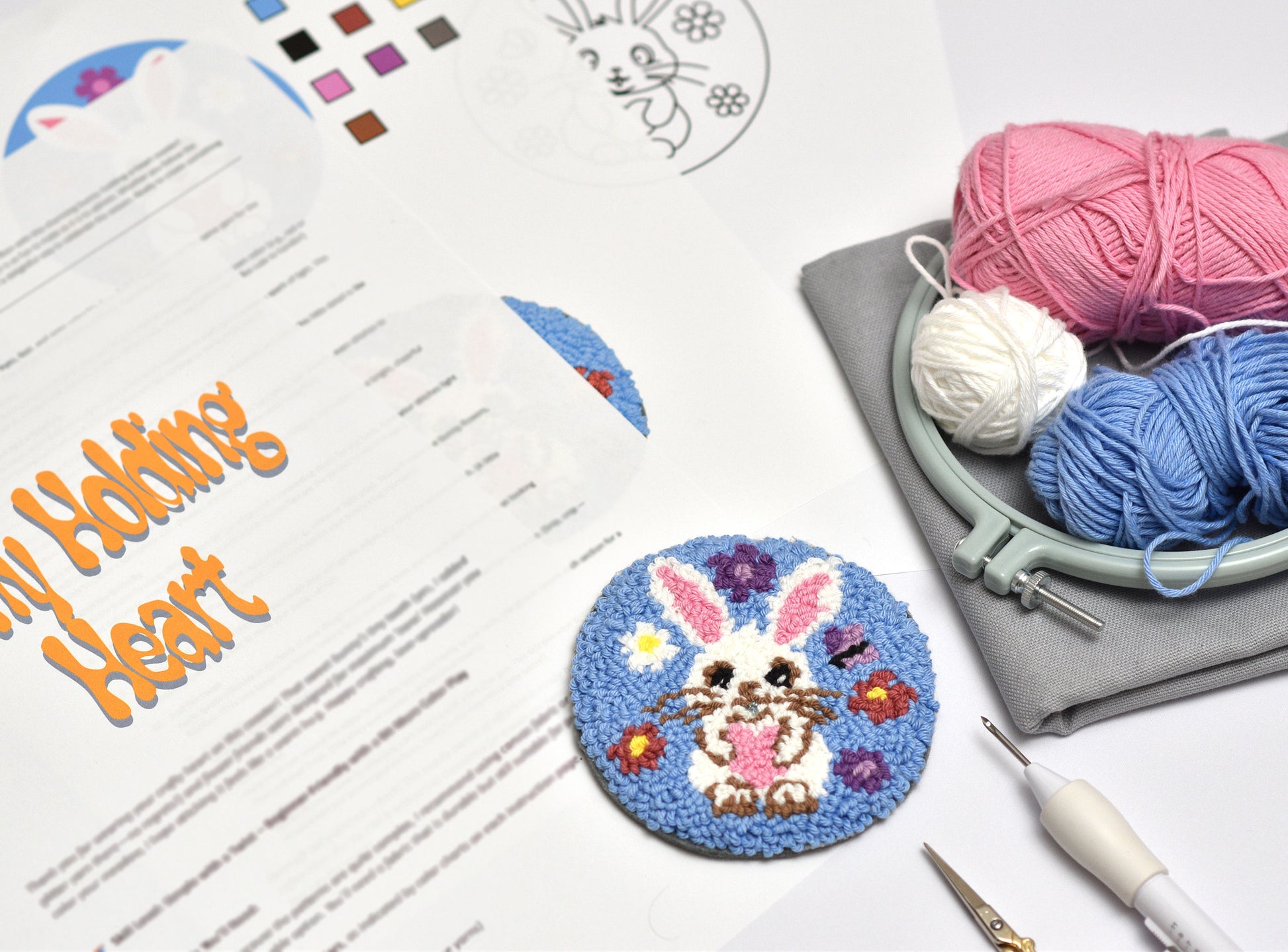 Embroidery hoop with yarn, completed embroidery coaster with Easter Bunny design, and design sheet on a white surface.